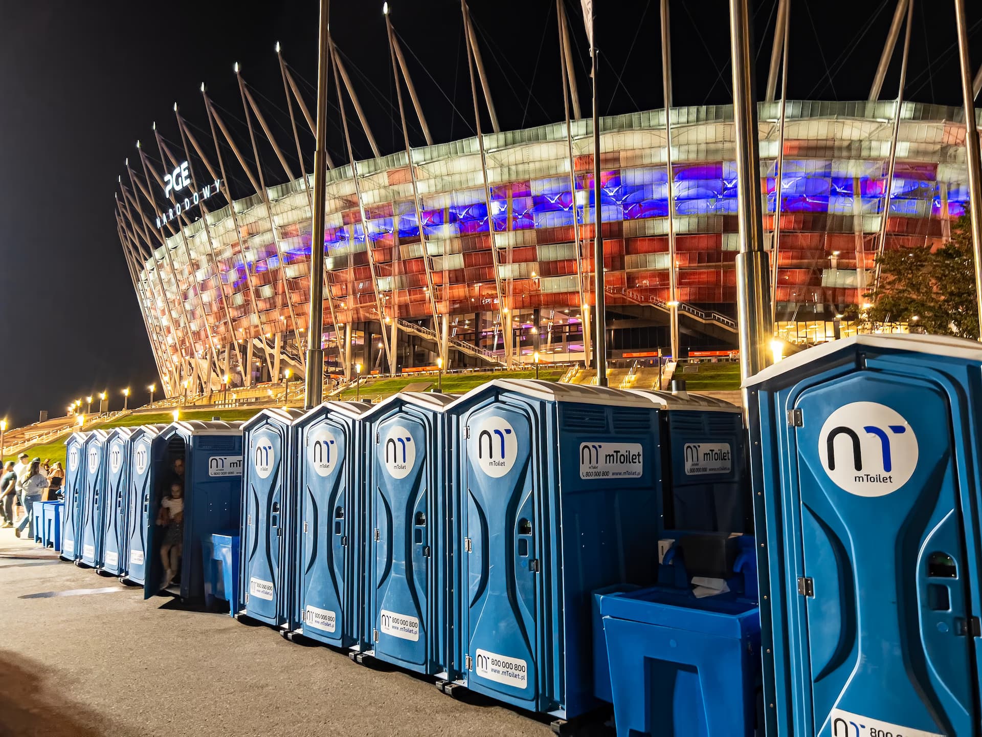 mToilet portatīvo tualešu rinda uz stadiona fona naktī
